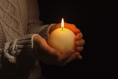 Photo of Young person holding burning candle in darkness, closeup