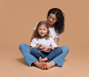 Beautiful mother with little daughter sitting on beige background