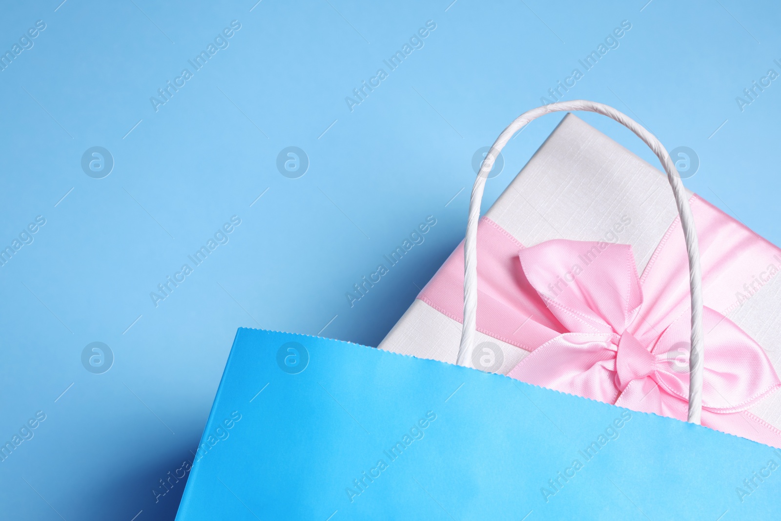 Photo of Bright paper shopping bag with gift box on light blue background, top view. Space for text