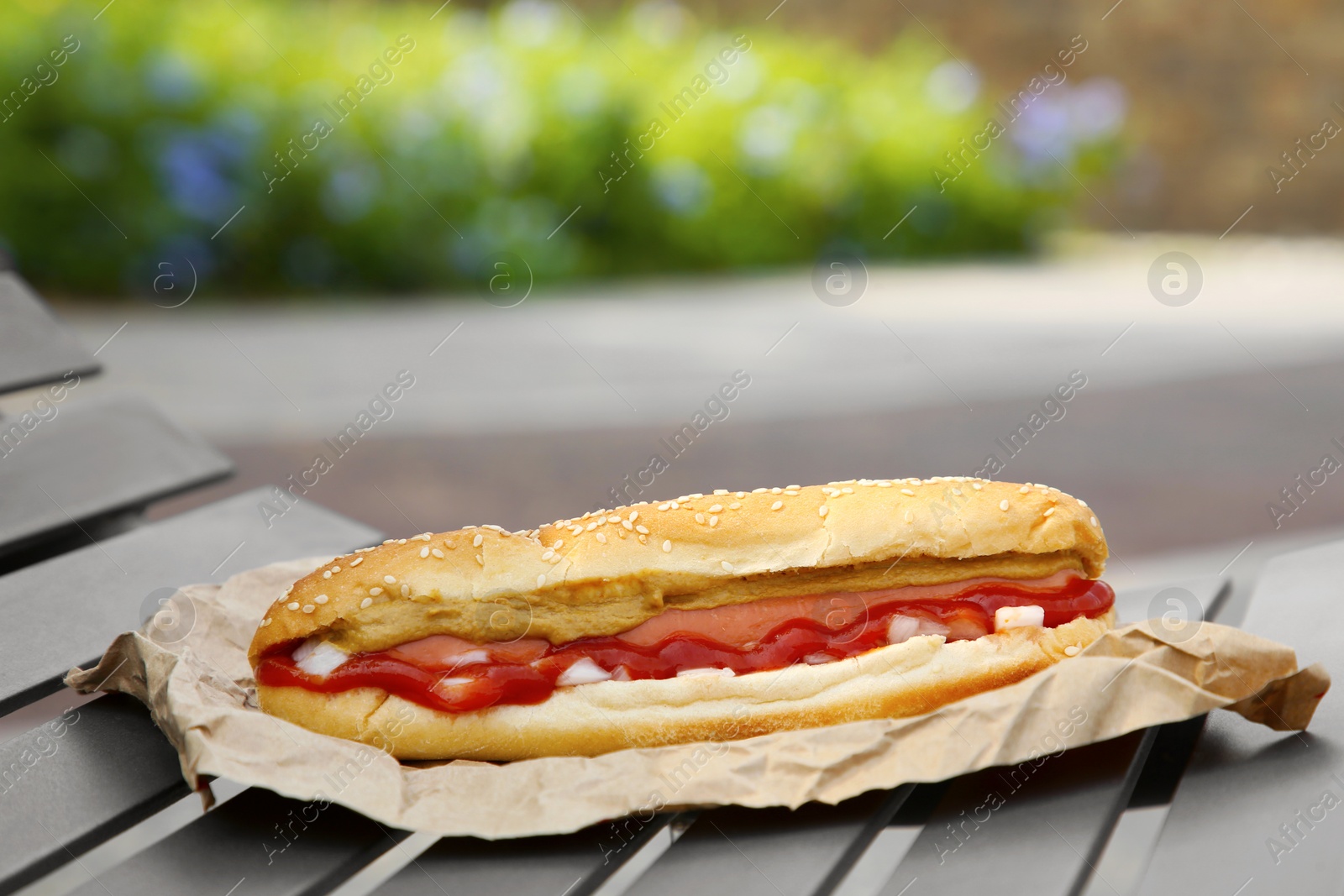 Photo of Fresh delicious hot dog with sauce on black bench outdoors