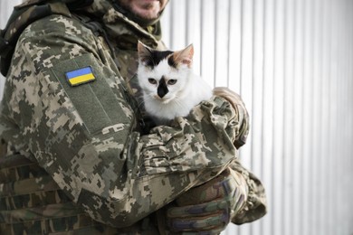 Photo of Ukrainian soldier with stray cat against light background, closeup. Space for text