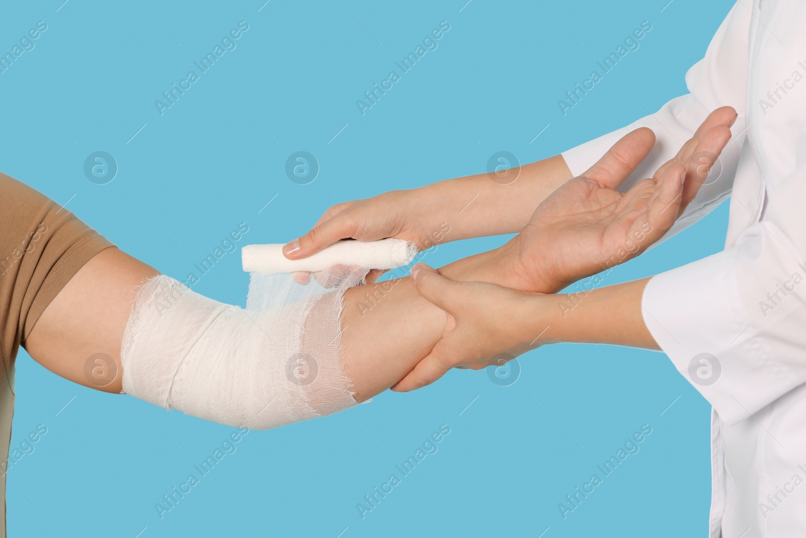 Photo of Doctor applying bandage onto patient's arm on light blue background, closeup