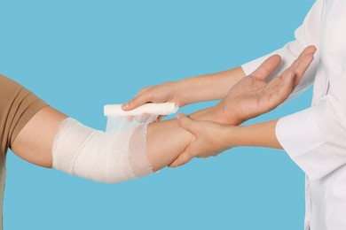 Photo of Doctor applying bandage onto patient's arm on light blue background, closeup