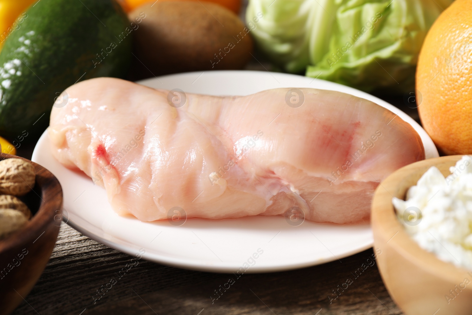 Photo of Healthy meal. Different vegetables and raw chicken breast on wooden table, closeup