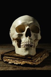 Human skull and old book on wooden table against black background