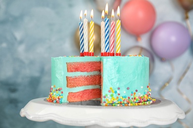 Fresh delicious birthday cake with candles on stand against color background