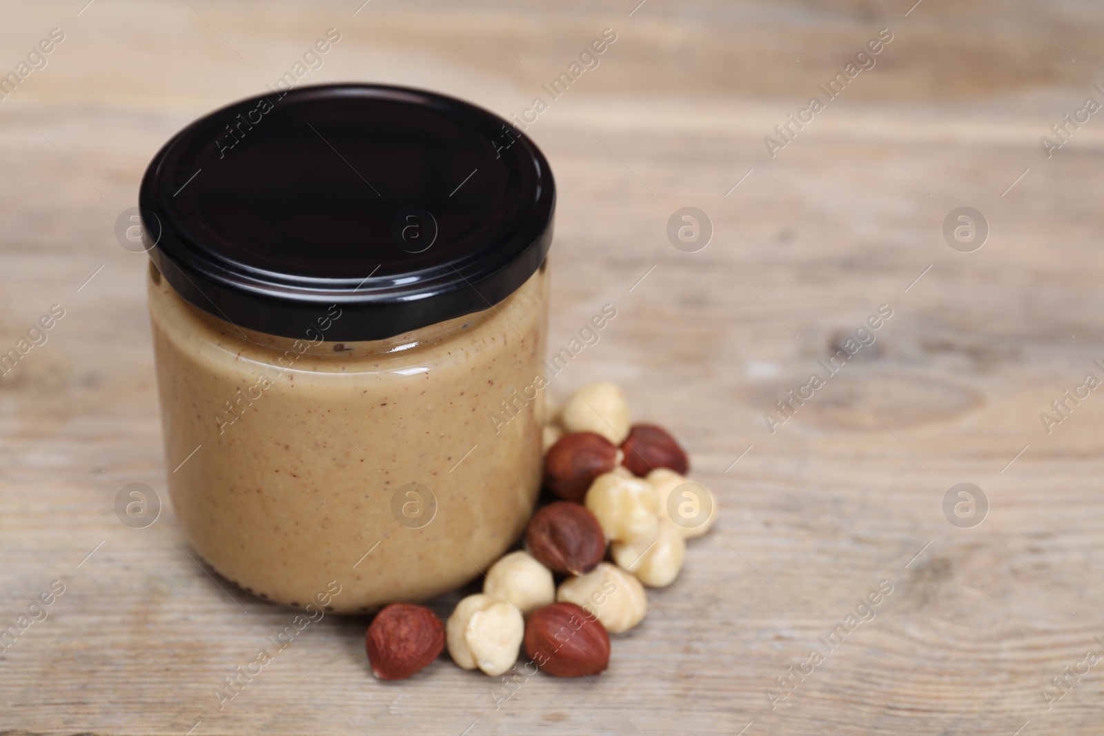 Photo of Tasty nut paste in jar and hazelnuts on wooden table, closeup. Space for text