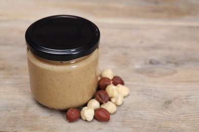 Photo of Tasty nut paste in jar and hazelnuts on wooden table, closeup. Space for text