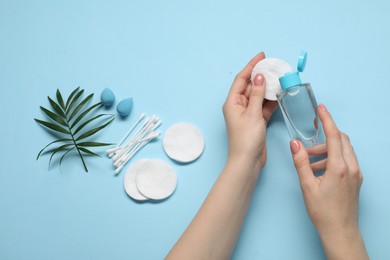 Photo of Woman using makeup remover, closeup. Sponges, cotton pads and buds on light blue background, top view