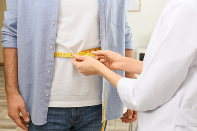 Photo of Young nutritionist measuring patient's waist in clinic, closeup