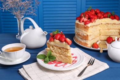 Piece of tasty cake with fresh strawberries, mint and cup of tea on blue wooden table