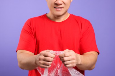 Photo of Man with bubble wrap on purple background, closeup