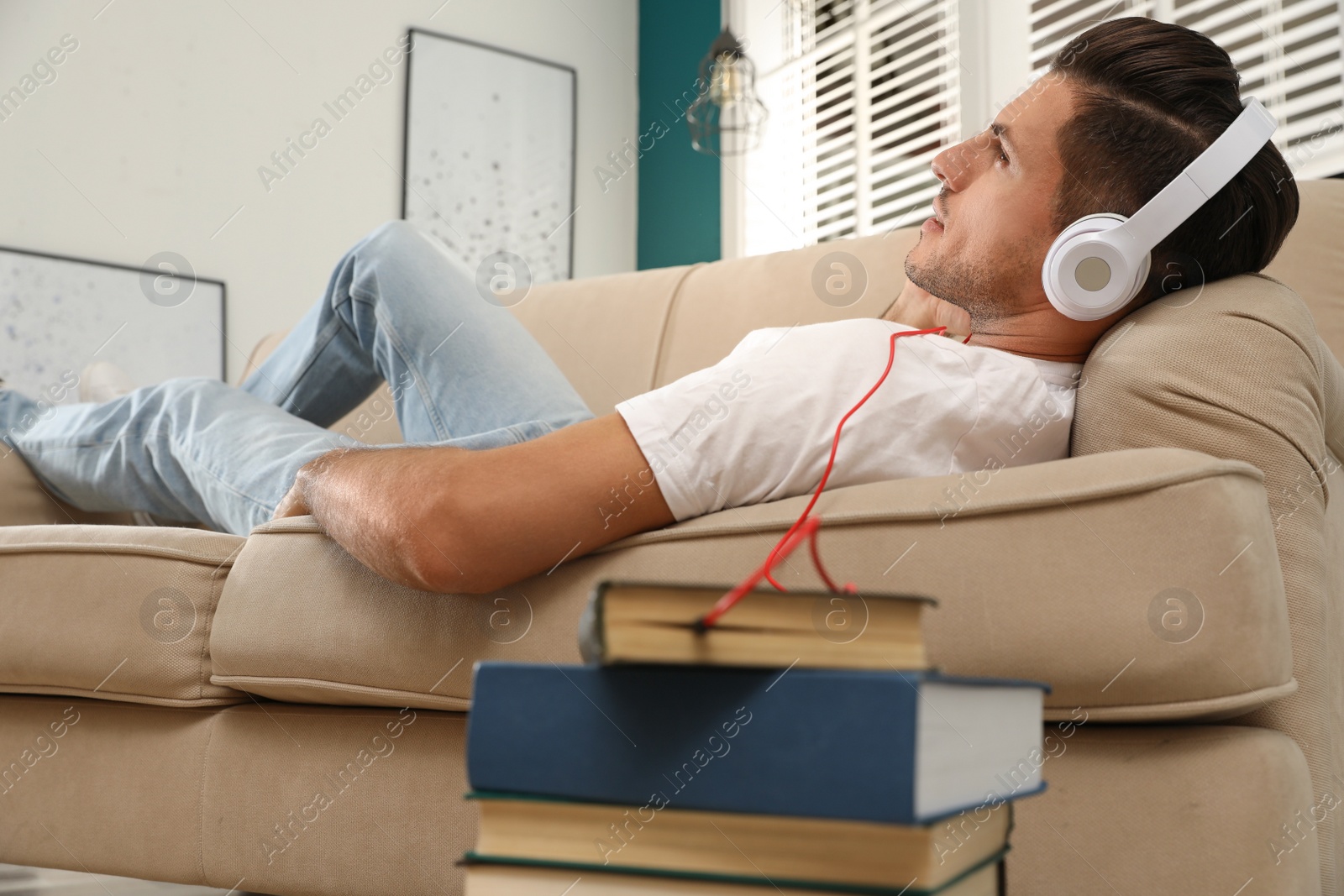Photo of Man with headphones connected to book
on sofa at home. Audiobook concept