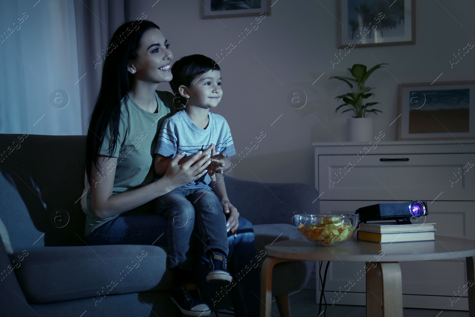 Photo of Young mother and her son watching movie using video projector at home
