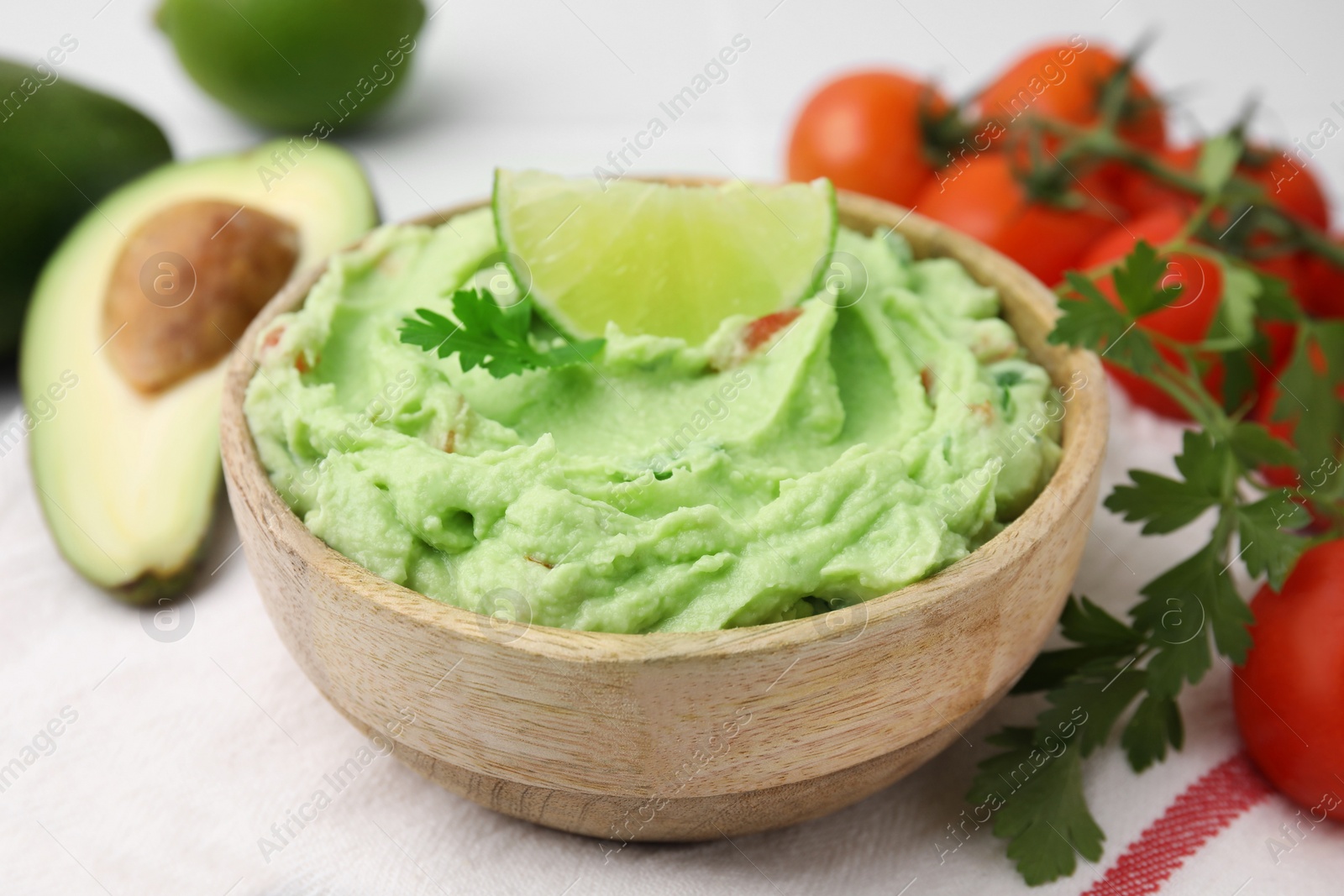 Photo of Bowl of delicious guacamole and ingredients on table, closeup