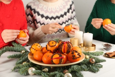 Photo of Friends decorating fresh tangerines with cloves at light wooden table, closeup. Making Christmas pomander balls
