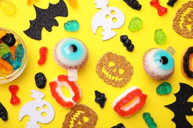 Photo of Tasty colorful jelly candies and Halloween decorations on yellow background, flat lay