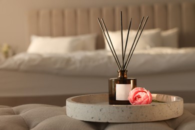 Photo of Aromatic reed air freshener and flower on bench in bedroom, space for text