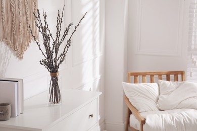 Photo of Glass vase with pussy willow tree branches on white chest of drawers in room, space for text