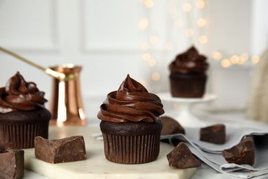 Photo of Delicious chocolate cupcake with cream on table against blurred lights. Space for text