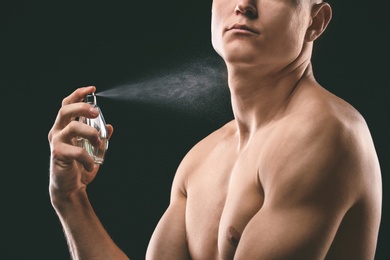 Handsome man using perfume on black background, closeup