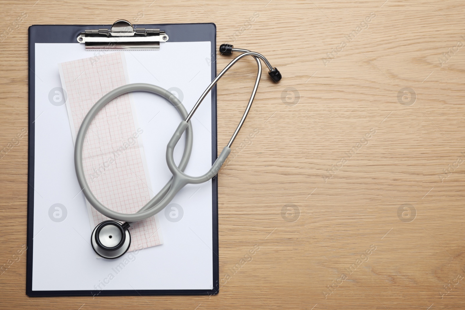 Photo of Clipboard with stethoscope and cardiogram on wooden table, top view. Space for text