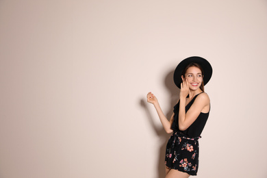 Young woman wearing floral print shorts and stylish hat on beige background. Space for text