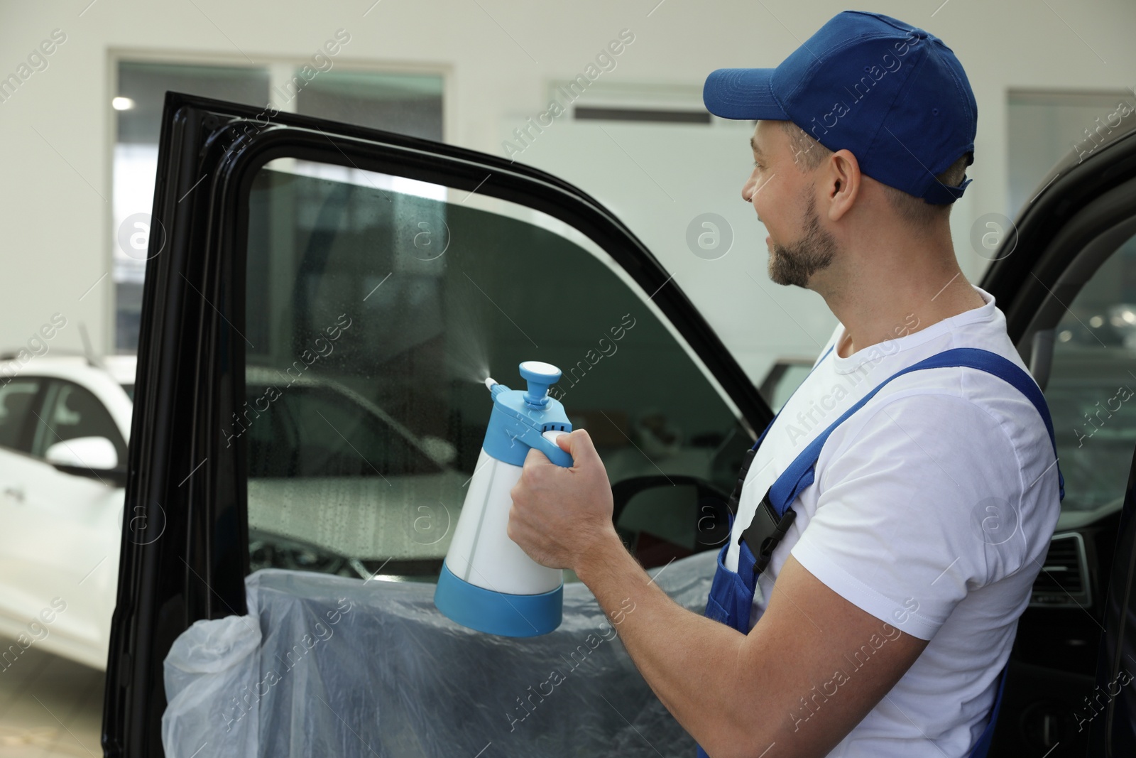 Photo of Worker spraying water onto tinted car window in workshop