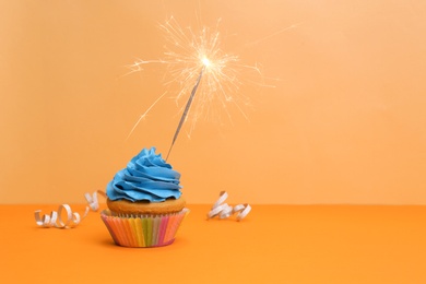 Birthday cupcake with sparkler on color background