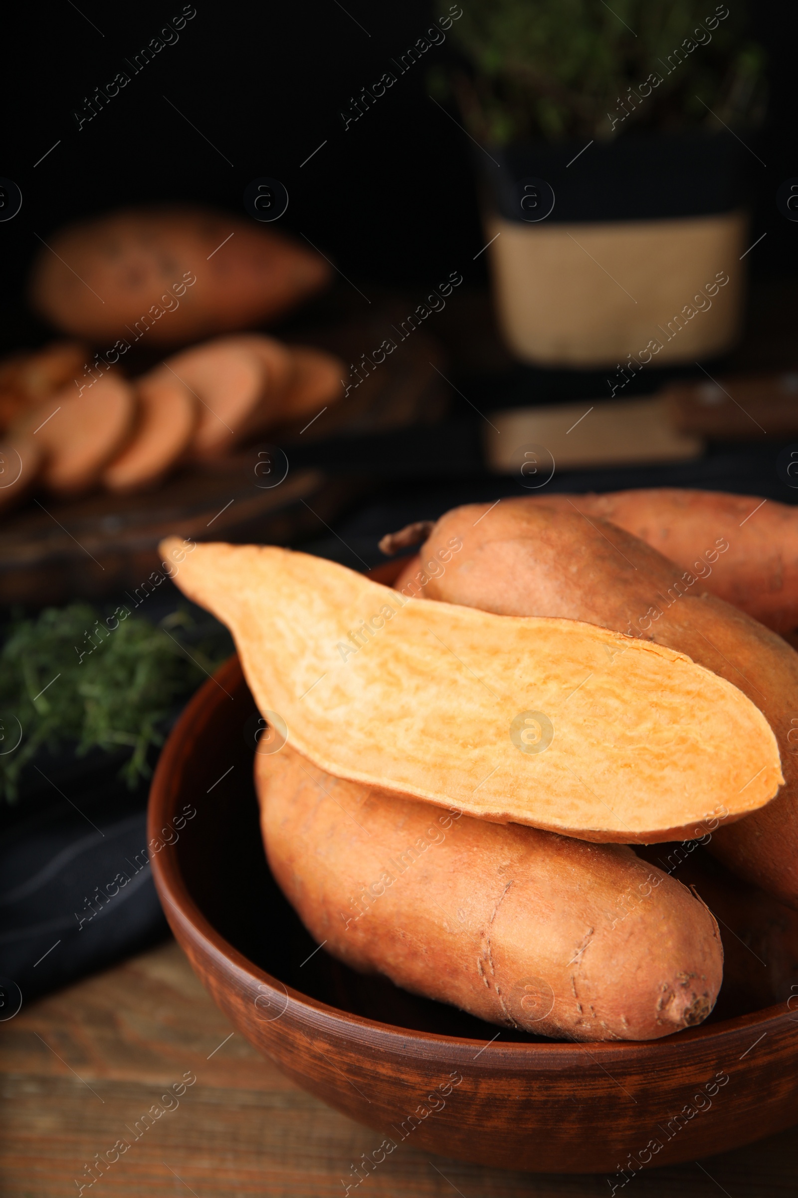 Photo of Cut and whole sweet potatoes in bowl on wooden table