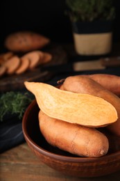 Photo of Cut and whole sweet potatoes in bowl on wooden table