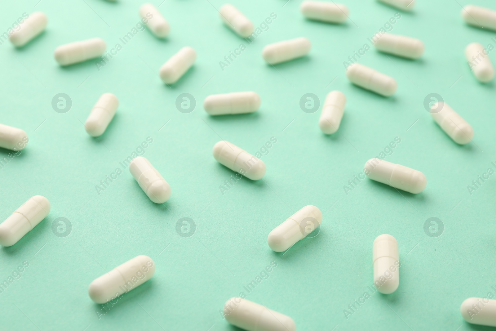 Photo of Many vitamin capsules on turquoise background, closeup