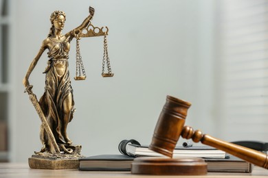 Photo of Figure of Lady Justice, gavel and notebooks on table indoors, space for text. Symbol of fair treatment under law