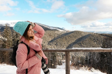 Young woman with backpack and camera enjoying mountain view during winter vacation. Space for text