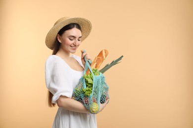 Woman with string bag of fresh vegetables and baguette on beige background, space for text