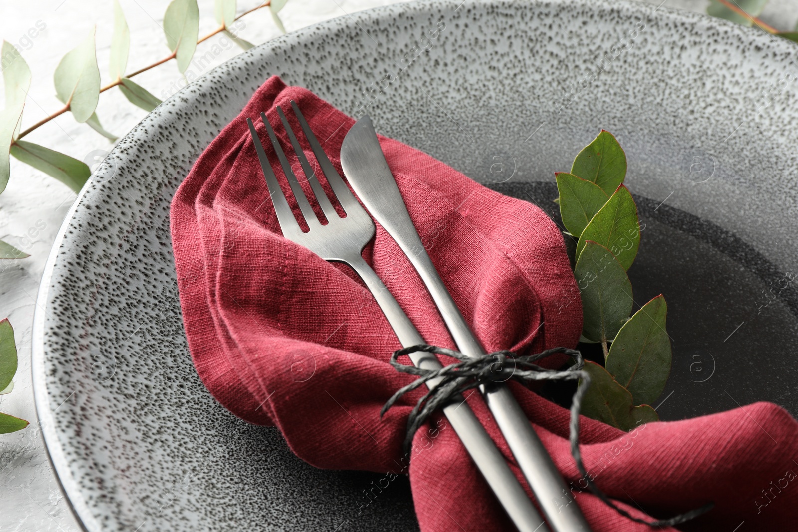 Photo of Stylish setting with cutlery, napkin, eucalyptus branches and plate on table, closeup