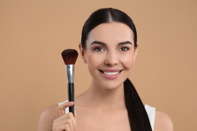 Photo of Portrait of beautiful woman with makeup brush on light brown background