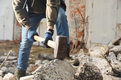 Photo of Man breaking stones with sledgehammer outdoors, closeup