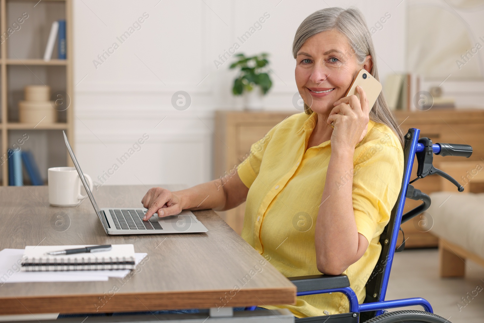 Photo of Woman in wheelchair talking on smartphone at table in home office