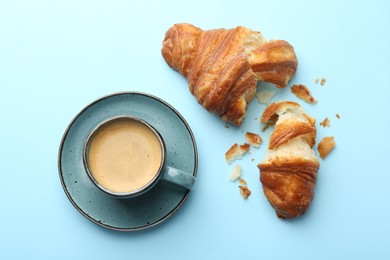 Photo of Delicious fresh croissant and cup of coffee on light blue background, flat lay