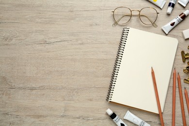 Flat lay composition with sketchbook and drawing tools on light wooden table, space for text