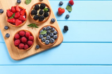 Tartlets with different fresh berries on light blue wooden table, flat lay and space for text. Delicious dessert