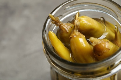 Photo of Glass jar with pickled peppers on grey table, closeup