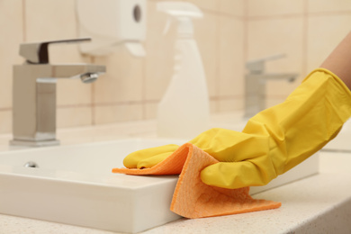 Photo of Woman cleaning sink with rag in bathroom, closeup