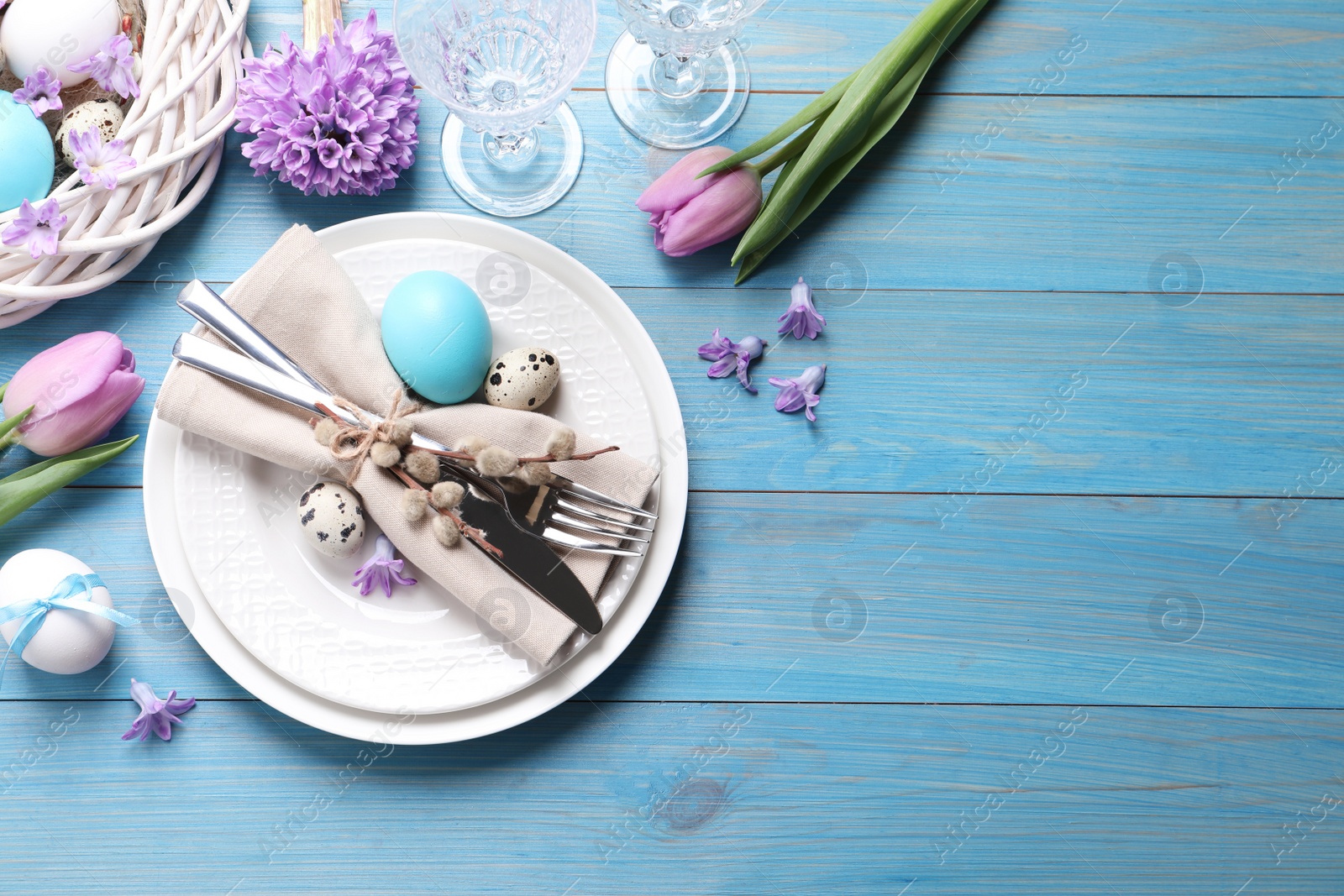 Photo of Festive Easter table setting with  painted eggs and floral decor on light blue wooden background, flat lay. Space for text