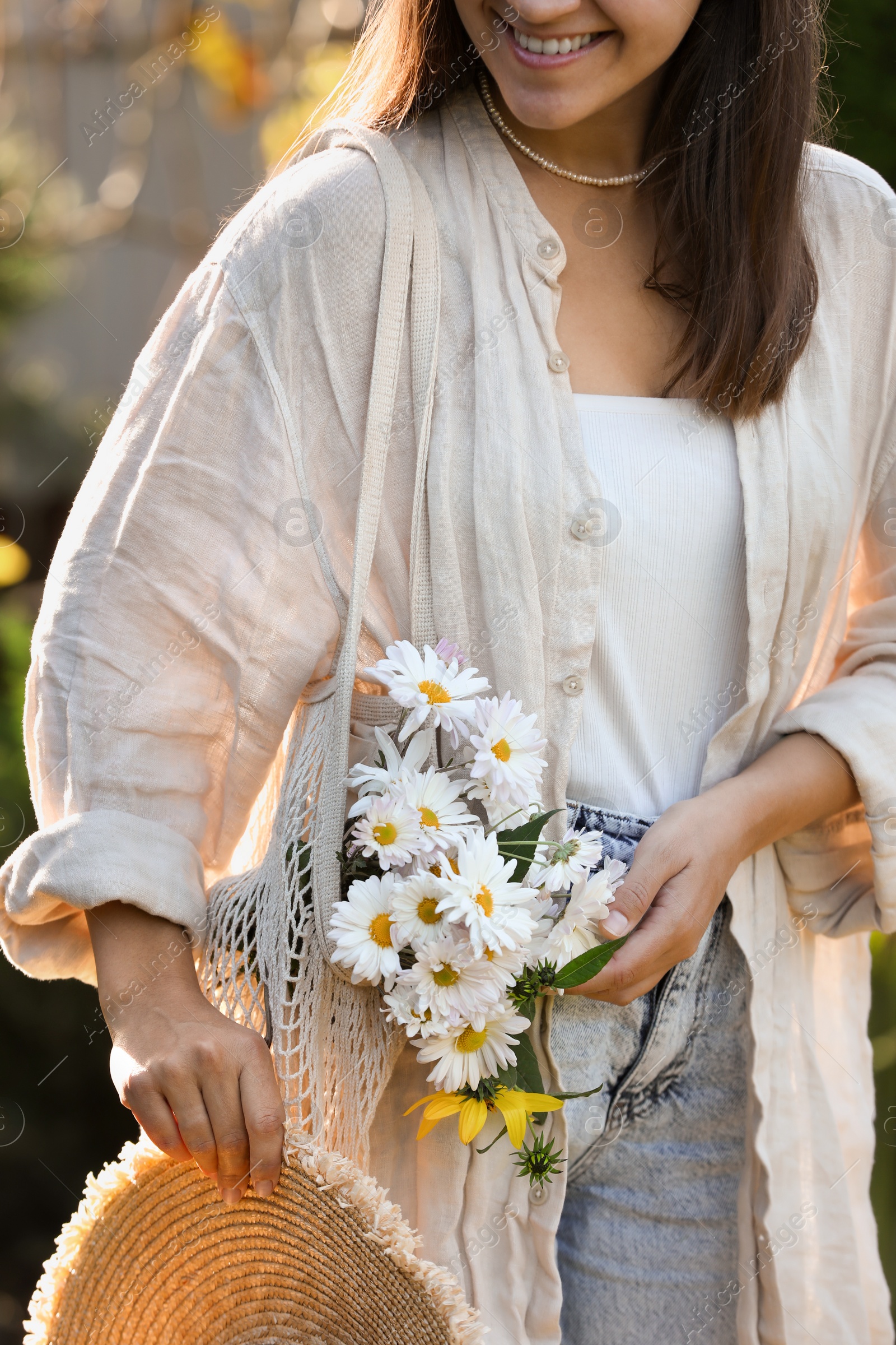 Photo of Woman holding net bag of beautiful white chamomile flowers outdoors, closeup