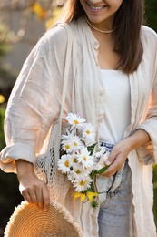 Photo of Woman holding net bag of beautiful white chamomile flowers outdoors, closeup
