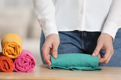 Photo of Woman rolling shirt at table indoors, closeup. Organizing clothes