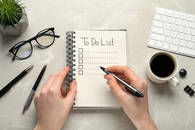 Woman filling To Do list in notepad at light grey marble table, top view