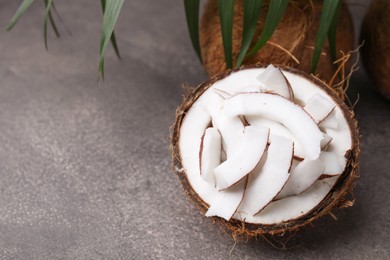 Coconut pieces in nut shell on brown table, space for text